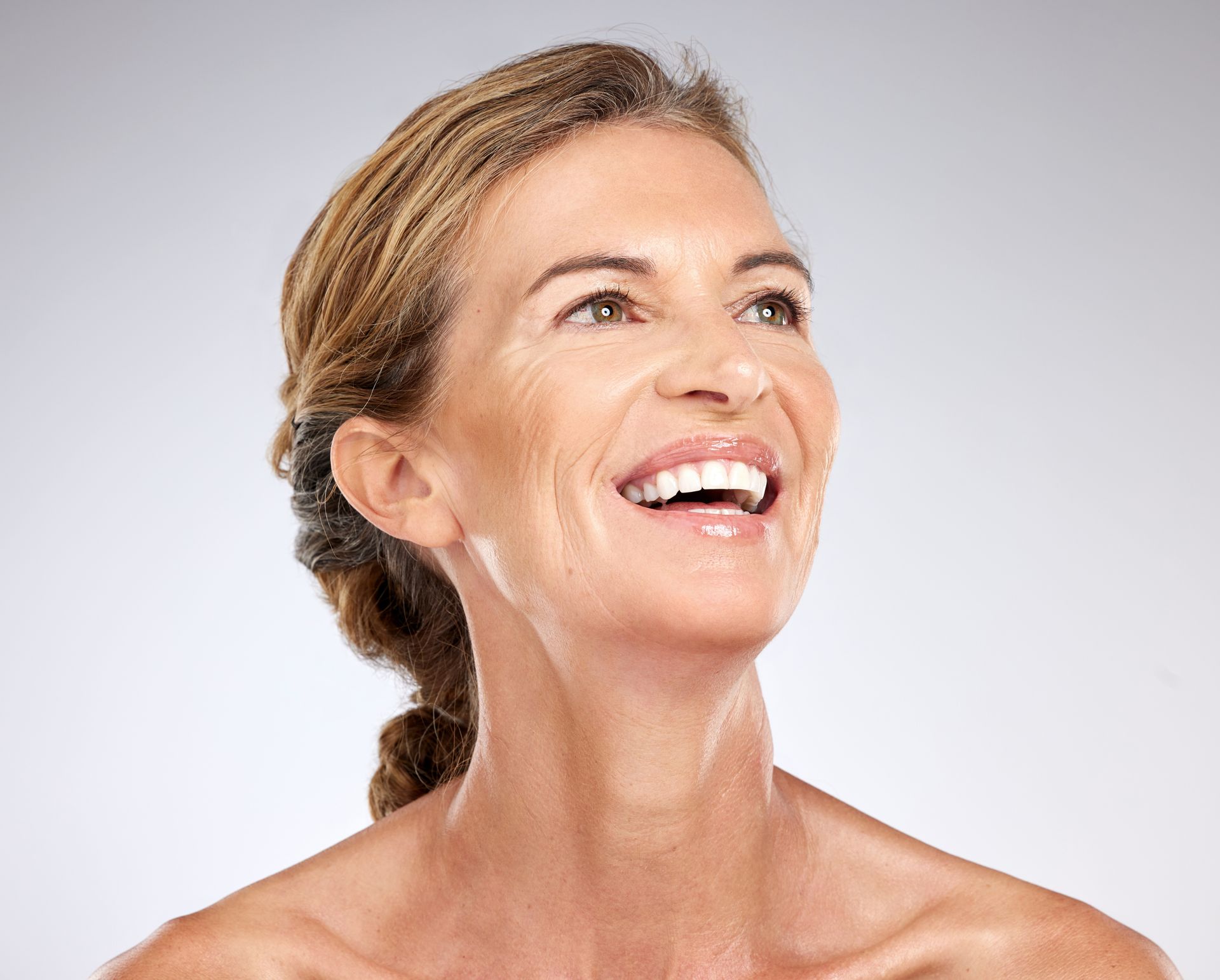 Woman with fair skin smiles, looking upwards. She has wrinkles, and her hair is pulled back.
