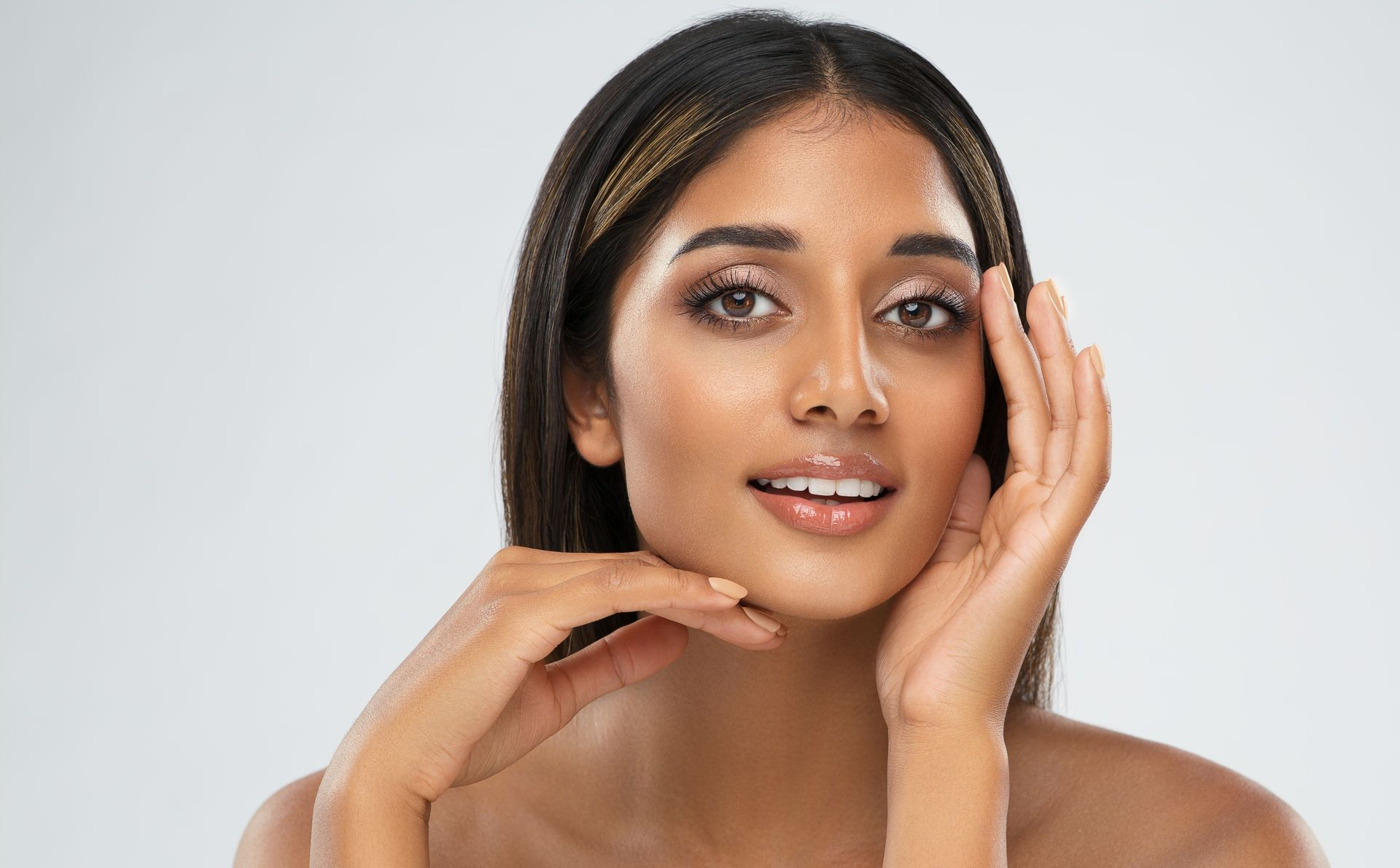 Woman with dark hair and skin, smiling, hands near face.