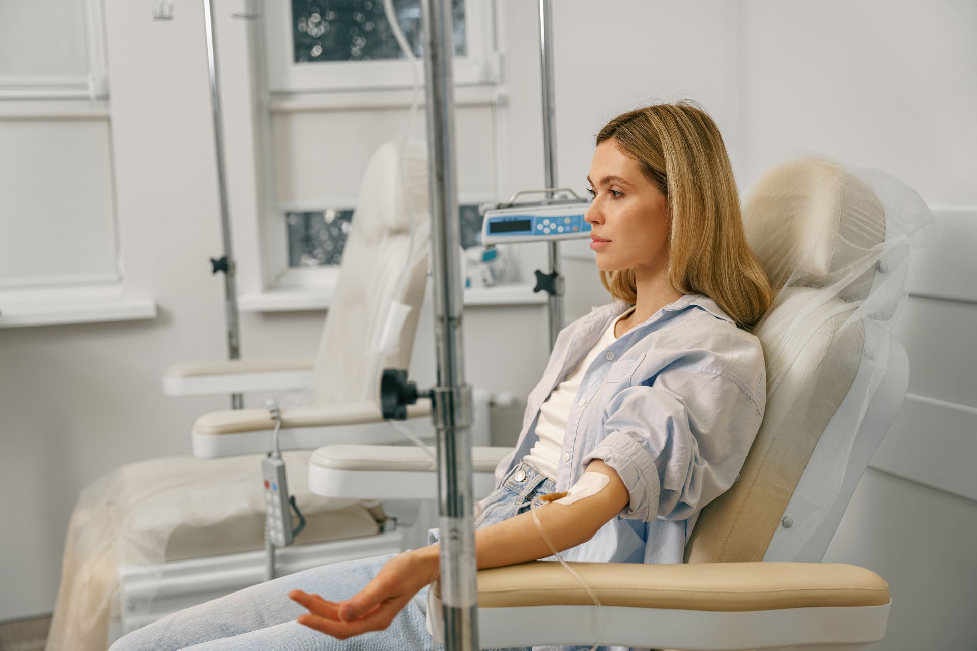 Woman receiving intravenous fluids in a medical chair, looking down.
