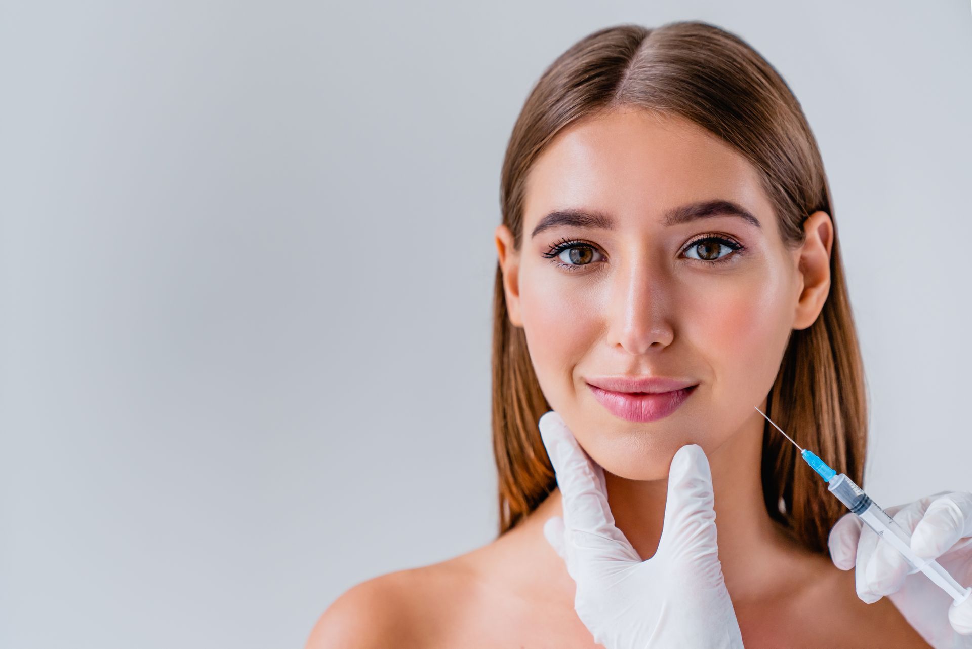Cosmetician holding a syringe near a woman’s face during a cosmetic injection procedure