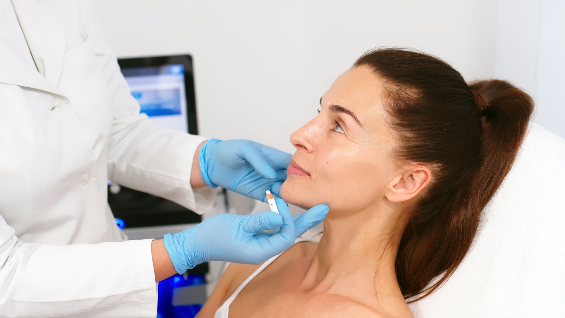 Woman receiving a facial injection from a medical professional wearing blue gloves in a clinic.