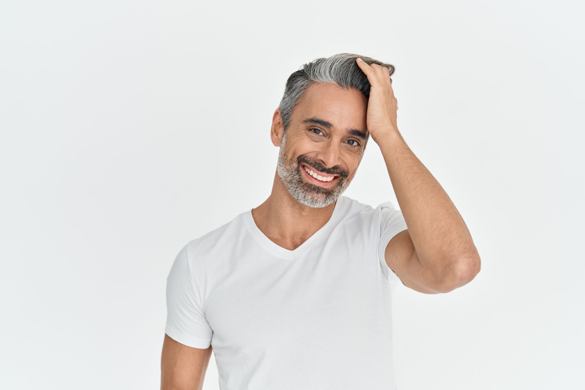 Man with graying hair, smiling, hand in hair, wearing white t-shirt, white background.