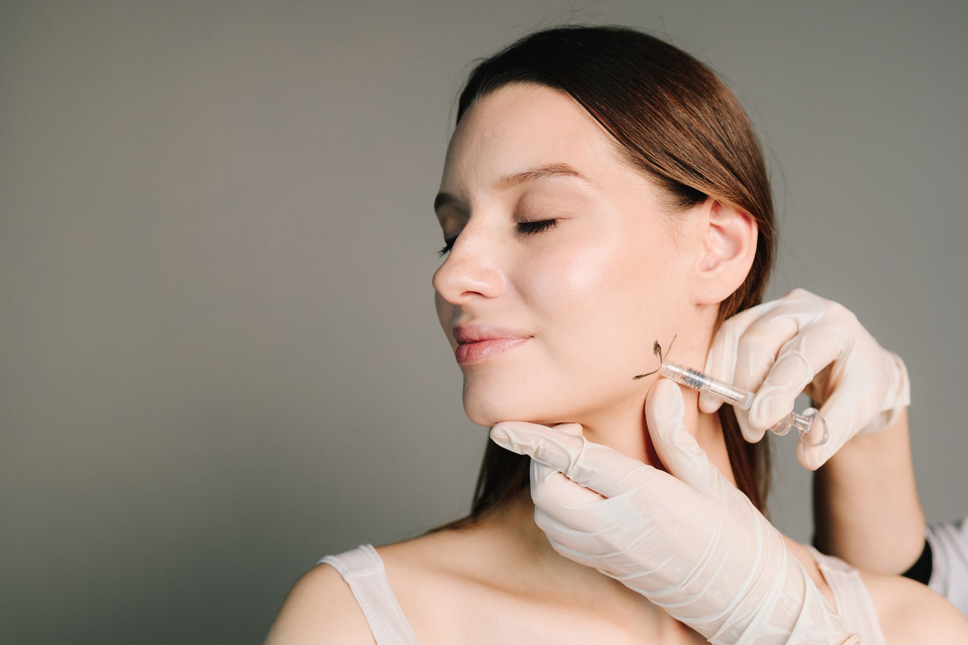 Woman receiving cosmetic injections in her face; a person wearing gloves injects with a syringe.