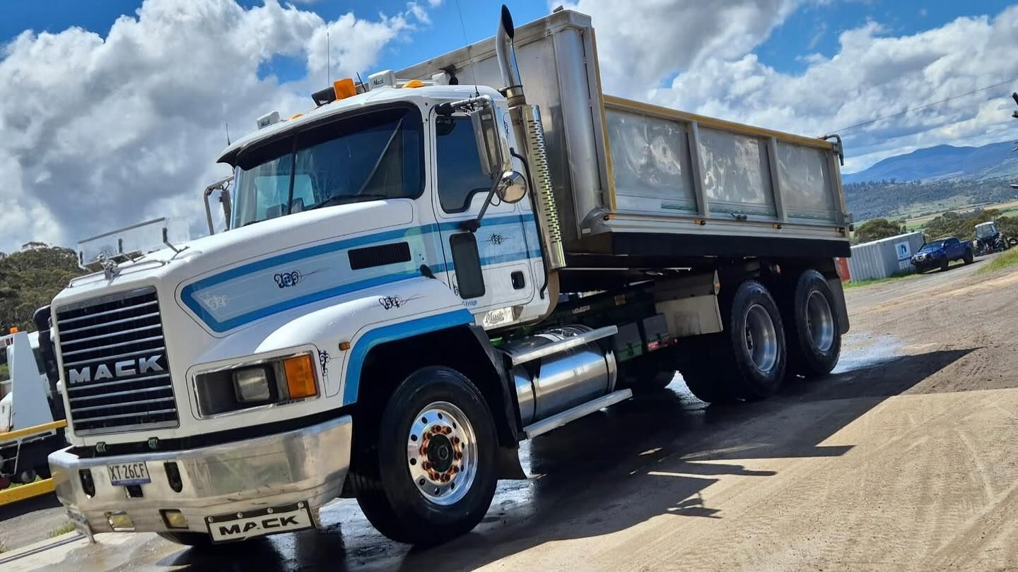 White and blue Mack dump truck parked outdoors on a sunny day.