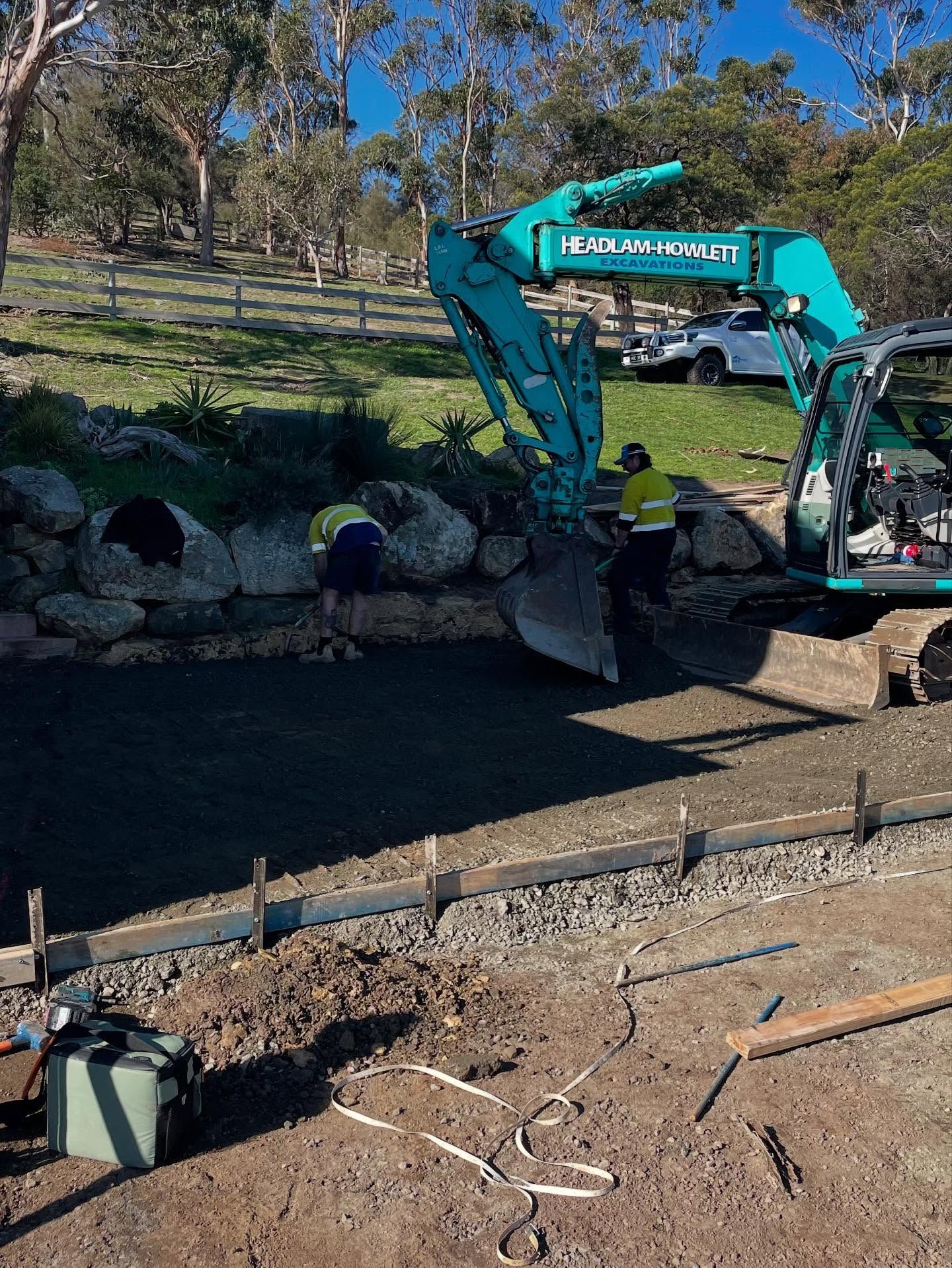 Excavator working on a construction site next to a concrete border, with a worker nearby.