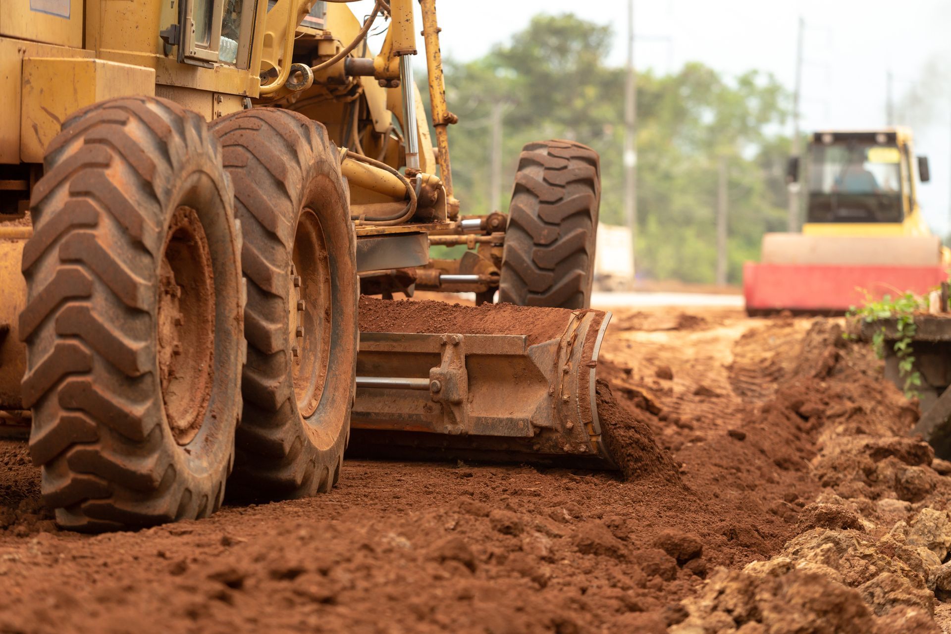 Close-up of heavy machinery leveling soil on a construction site with a roller in the background.