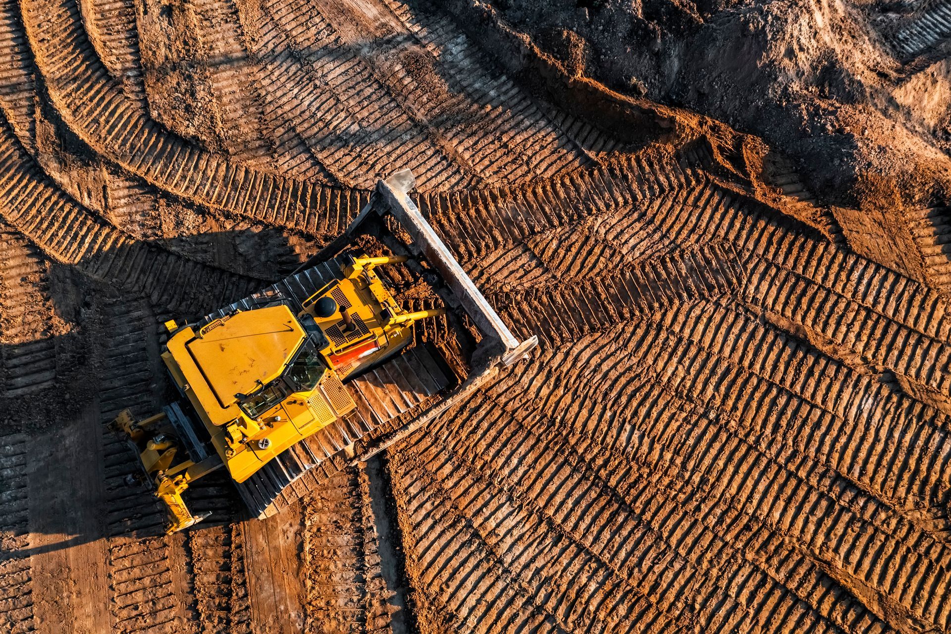 Yellow bulldozer grading soil on a construction site with visible tracks across the ground.