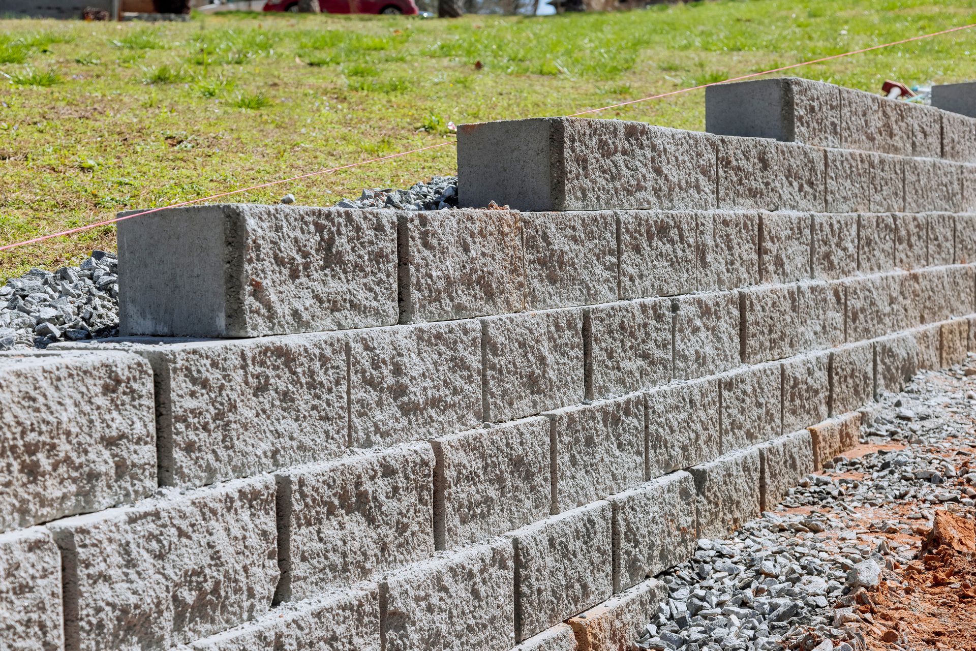 Gray concrete retaining wall with gravel base, built on a gentle slope with grass in the background.