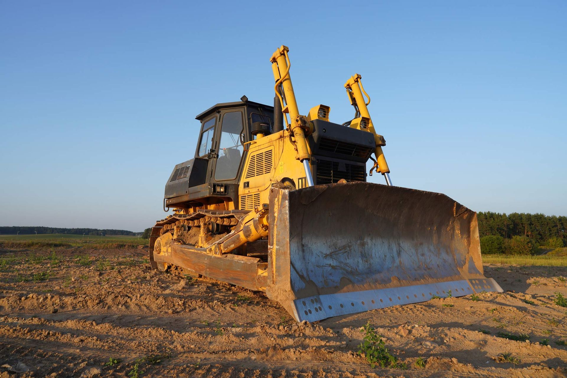 Yellow bulldozer on dirt field under clear sky, used for earthmoving construction work. Yellow bulldozer on dirt field under clear sky, used for earthmoving construction work.
