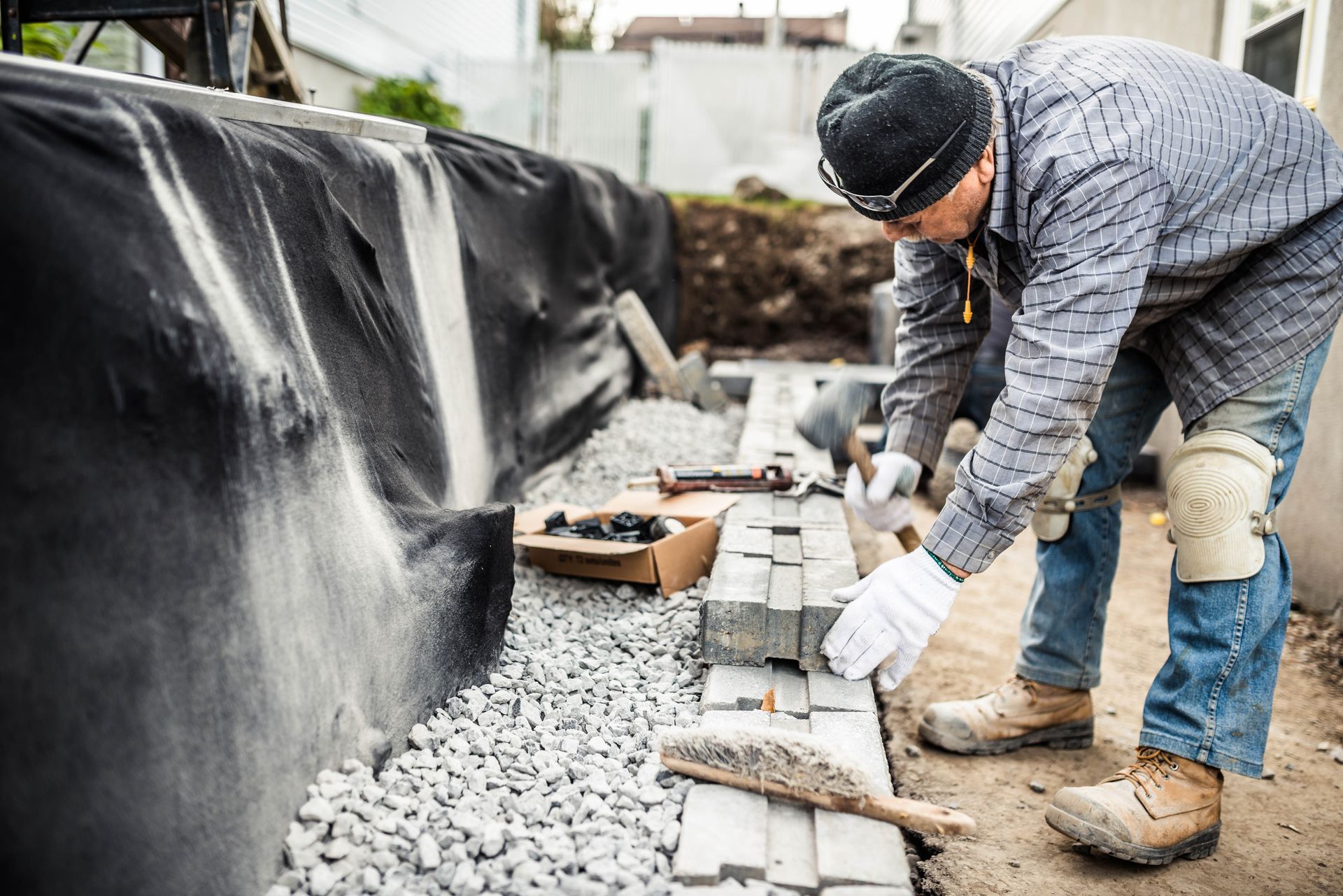 Construction worker laying bricks on gravel path with tools and materials nearby. Construction worker laying bricks on gravel path with tools and materials nearby.