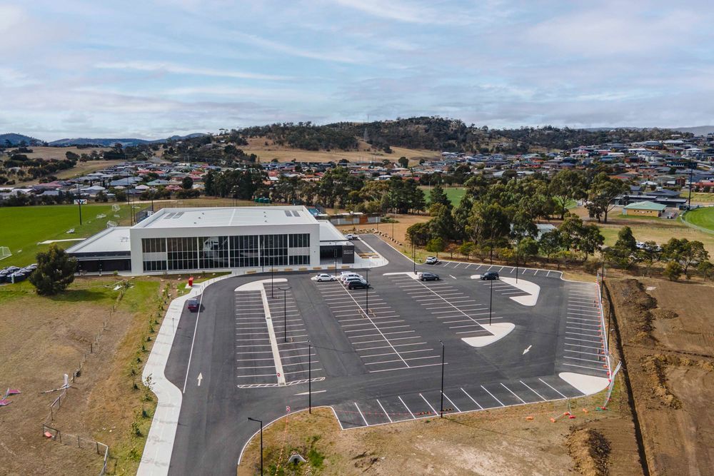 Aerial view of a modern, two-story building with a large parking lot and a town in the background.