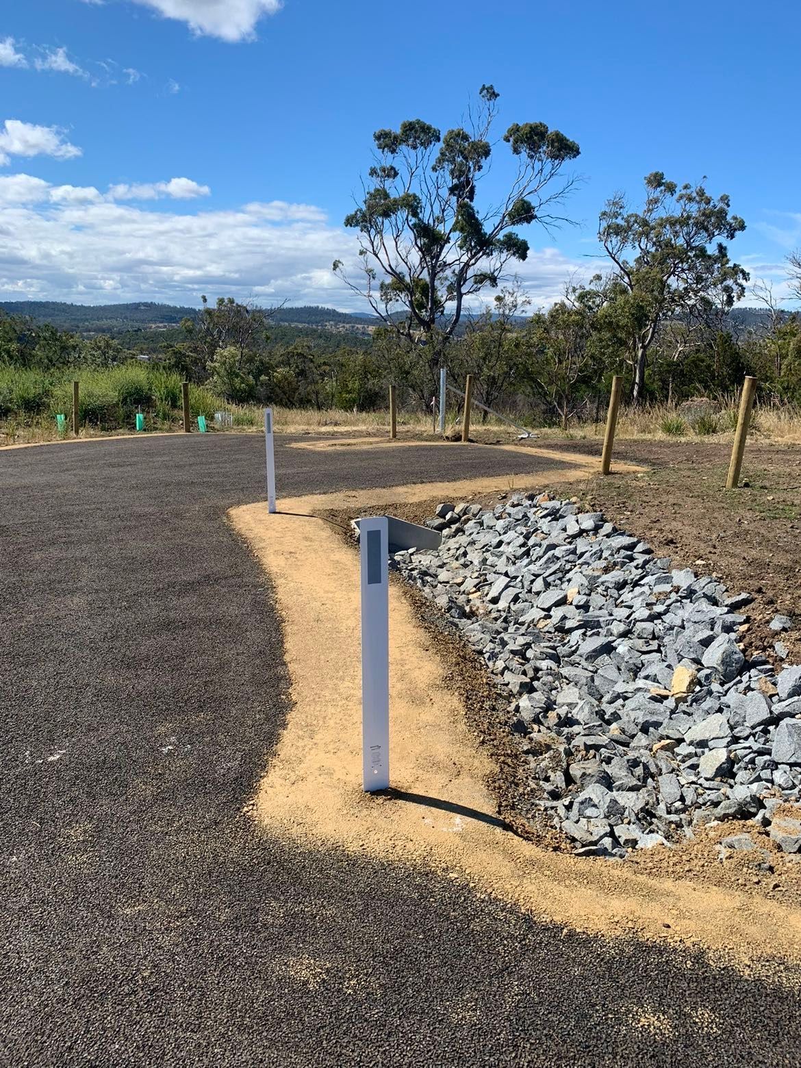 Gravel path leading through a landscape with white posts, rock border, and trees under a blue sky.