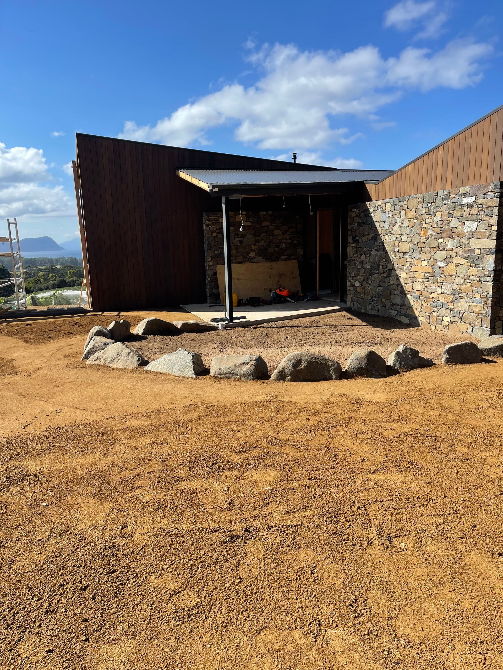 A modern building with a stone facade and rusty metal siding on a dirt lot under a blue sky.