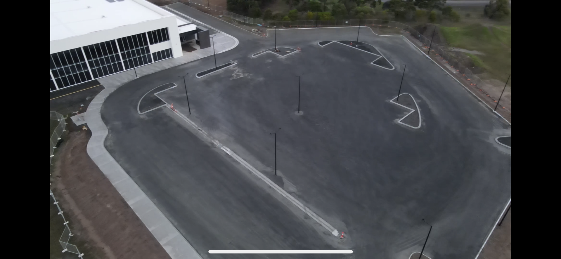 Aerial view of an empty parking lot next to a modern building. Black asphalt and white markings are visible.