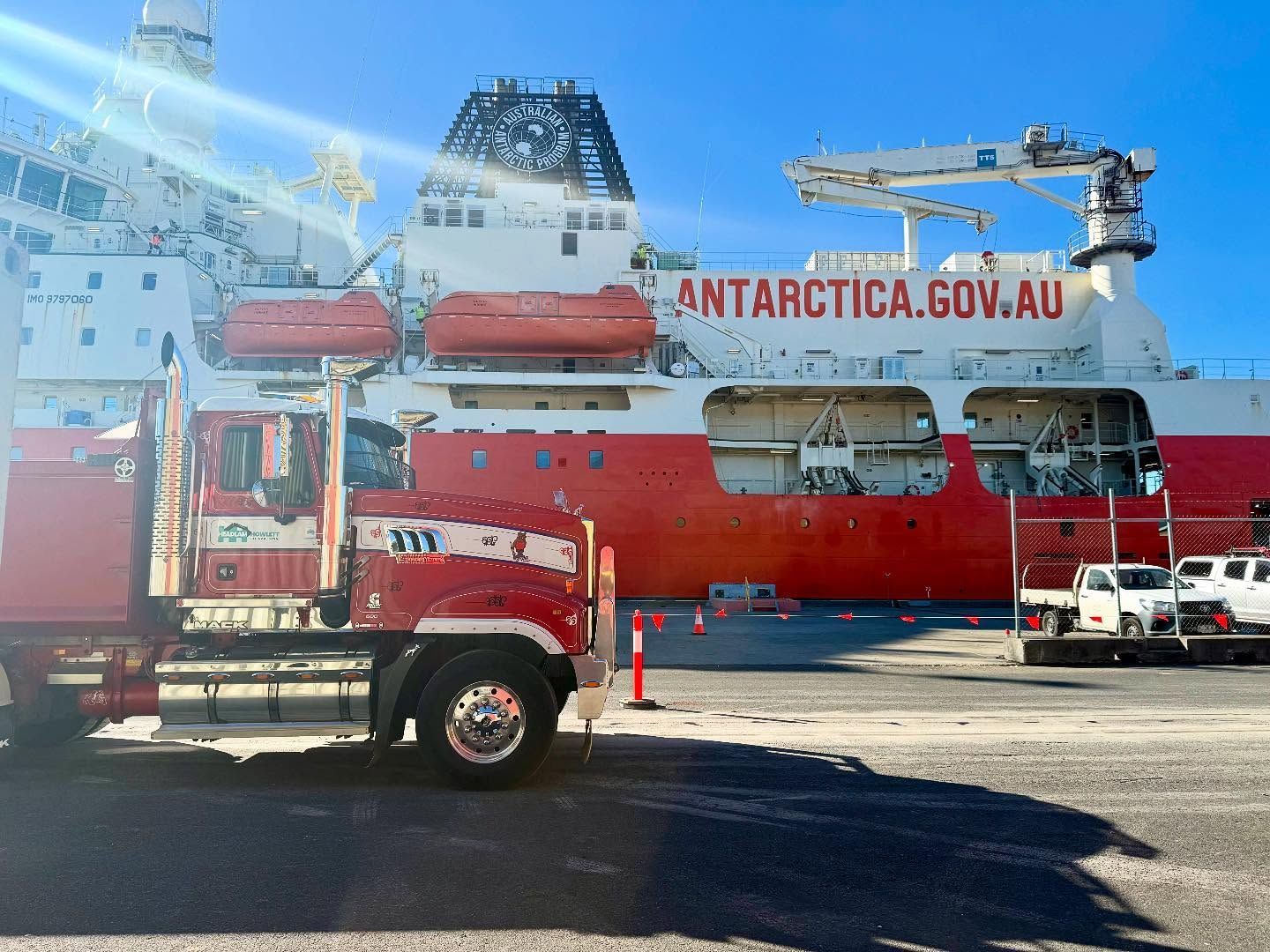 A red and white Australian Antarctic supply ship docked with a truck.