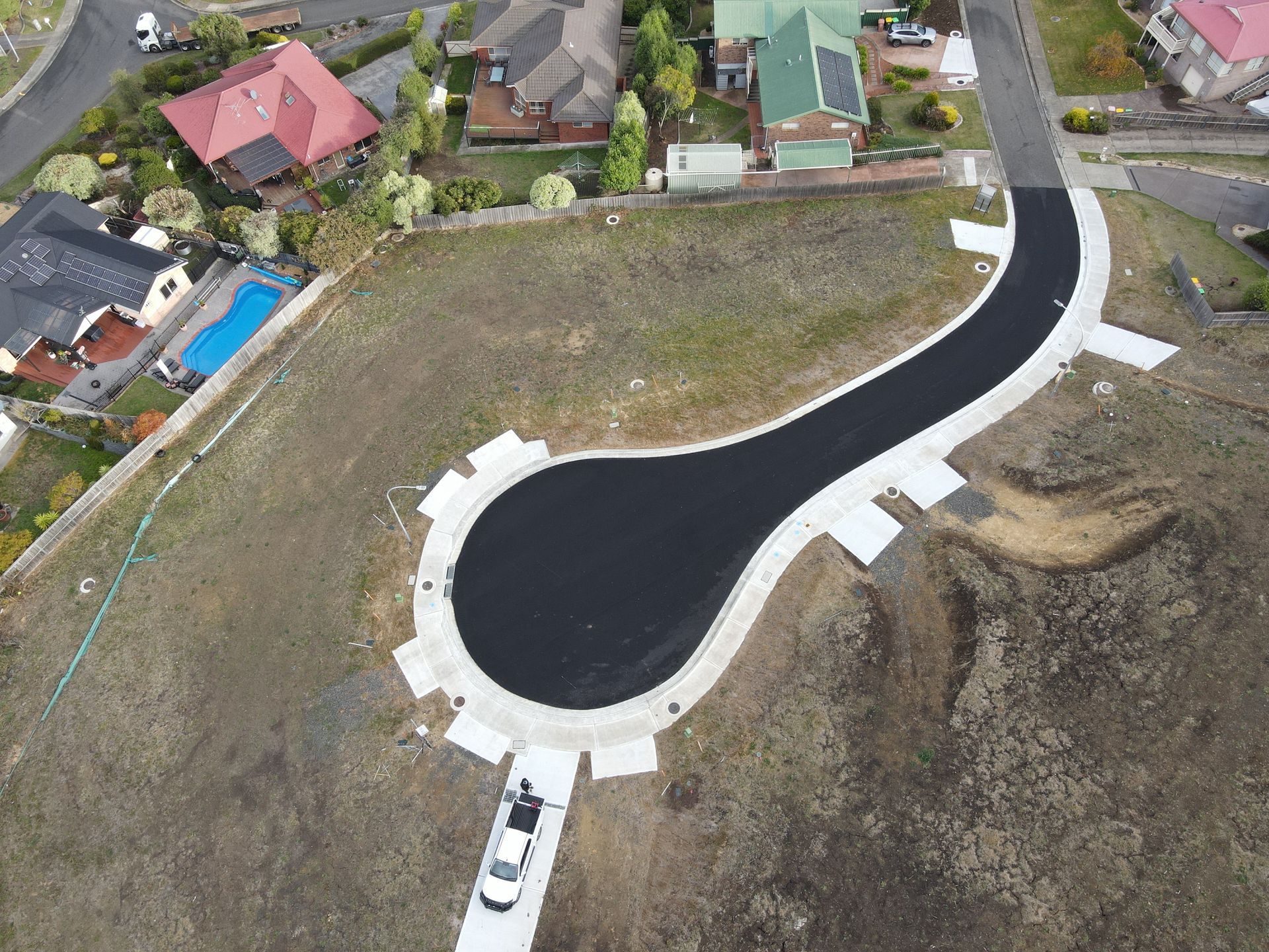 Aerial view of a newly paved road in a residential area, with a car parked at the end and surrounding houses.