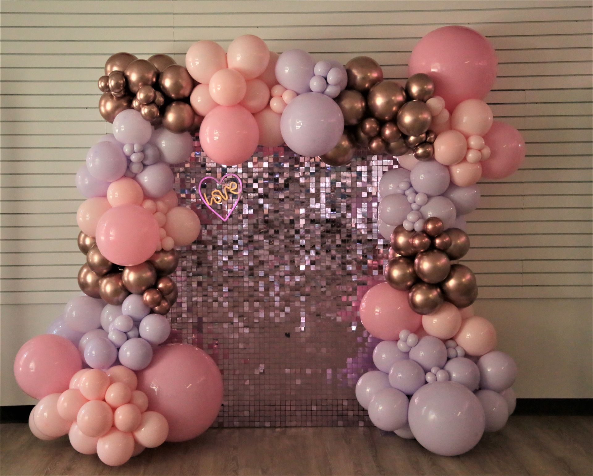 A wall covered in pink , purple , and gold balloons.