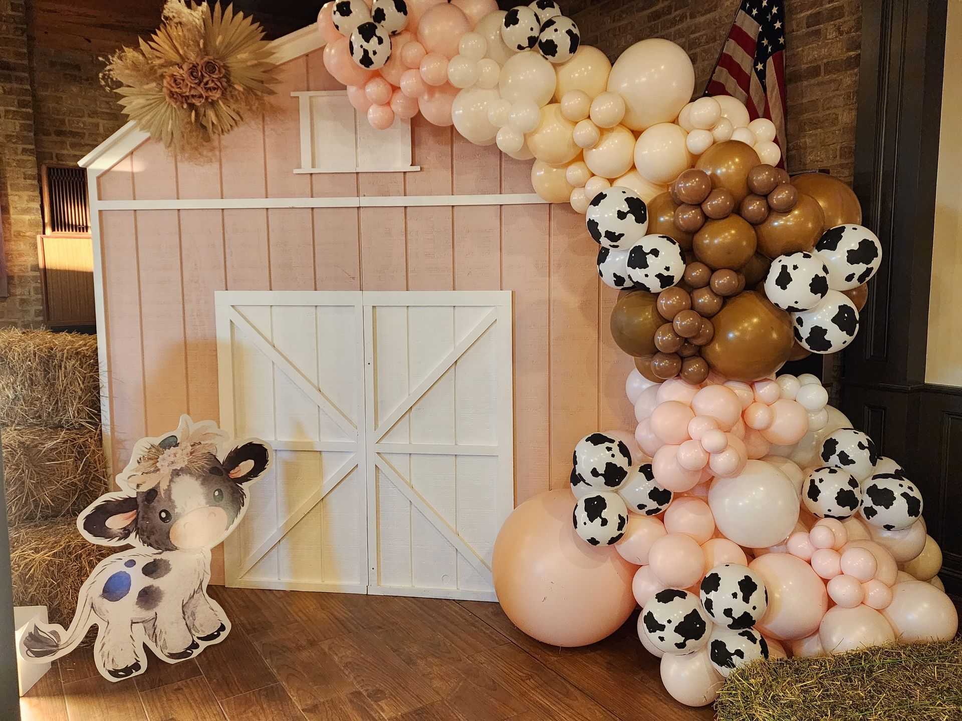 A cow is standing in front of a barn decorated with balloons.