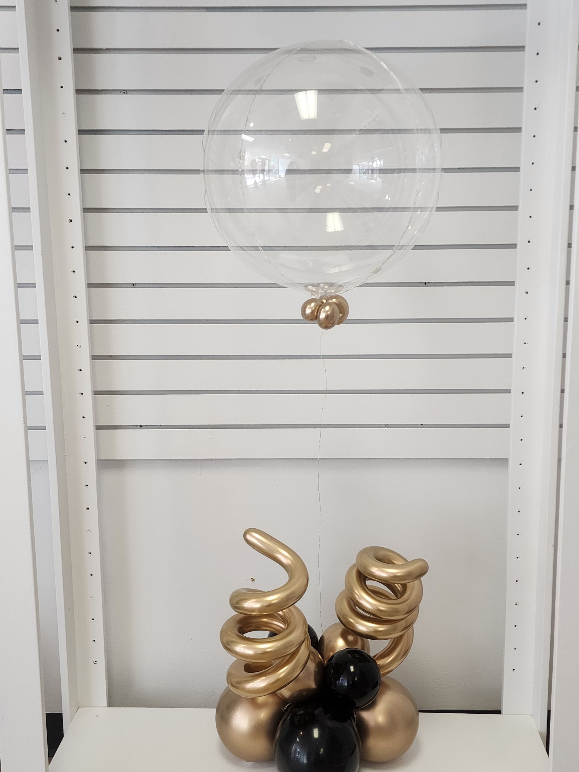 A clear balloon is sitting on top of a table with gold and black balloons.