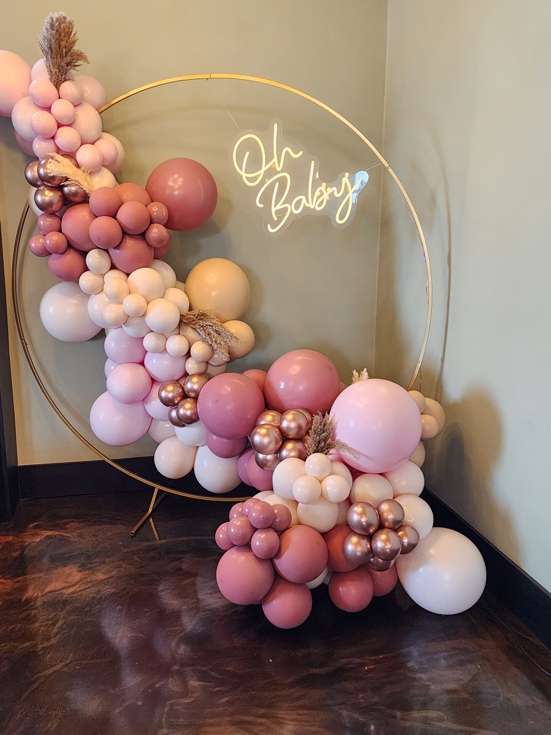 A hoop filled with pink and white balloons and a neon sign that says oh baby.