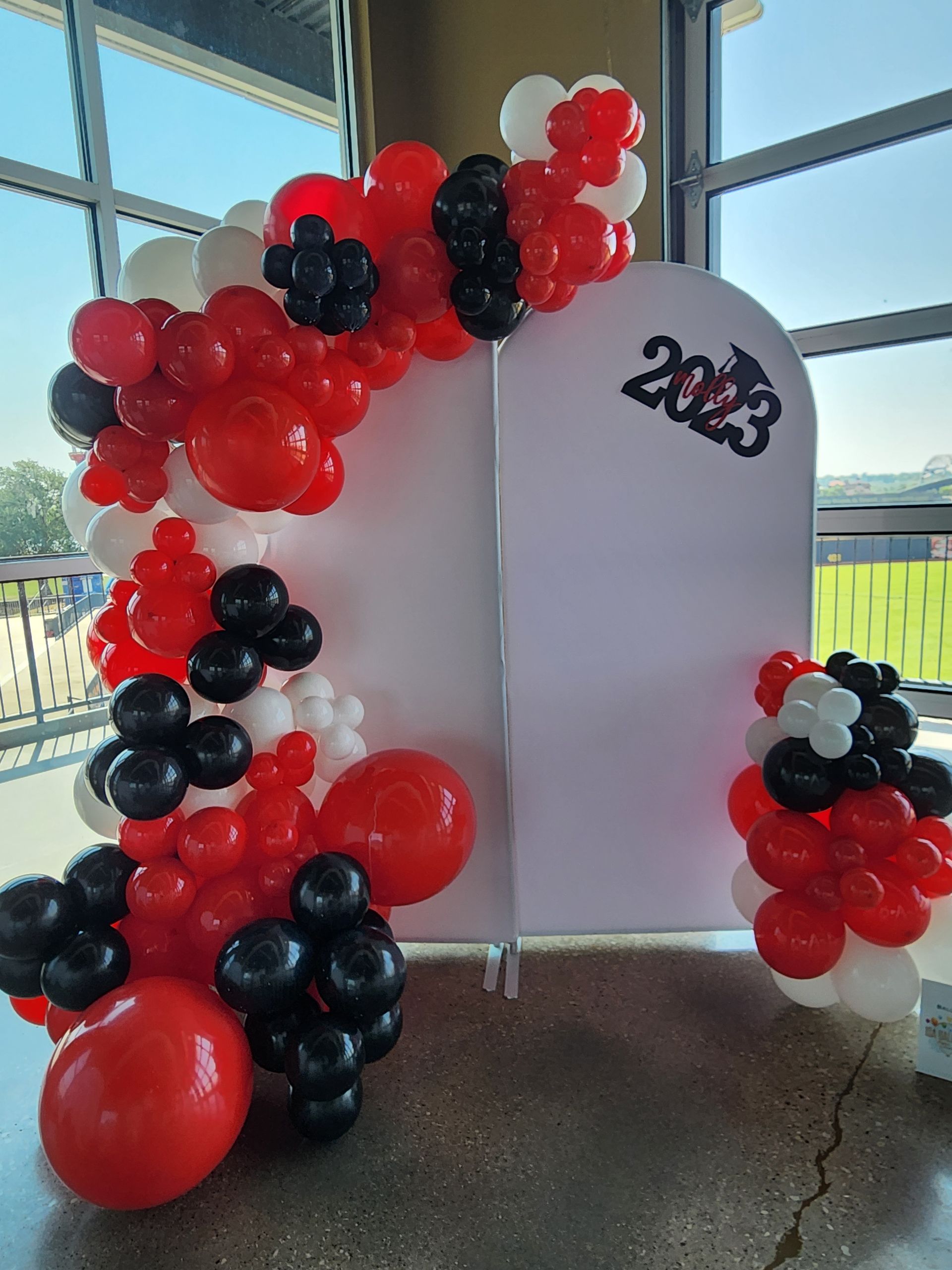 A wall covered in red , white and black balloons with the year 2023 on it.