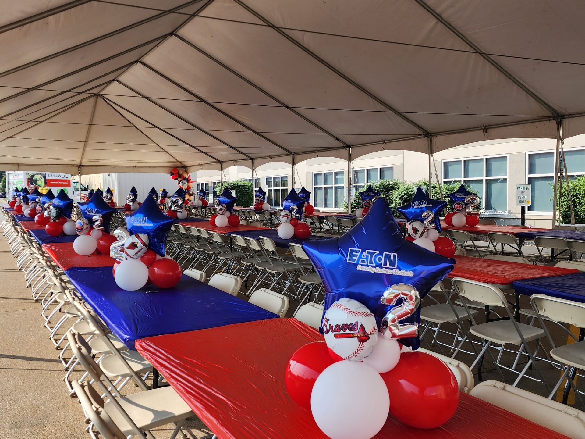 Tables and chairs under a tent decorated with red white and blue balloons