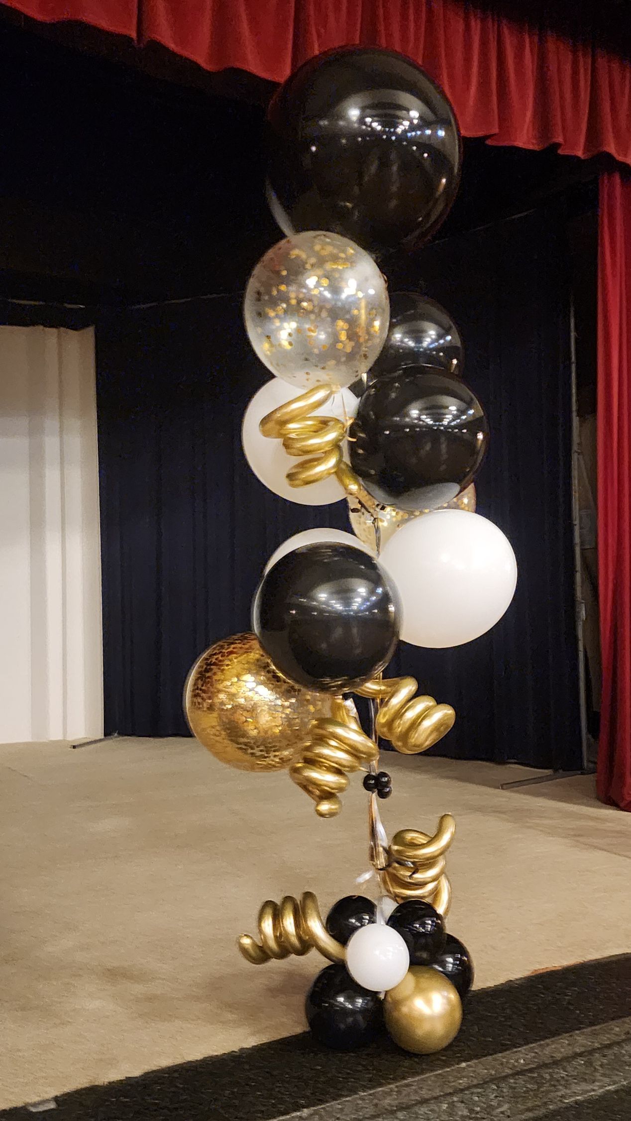 A bunch of black , white and gold balloons are sitting on a stage.