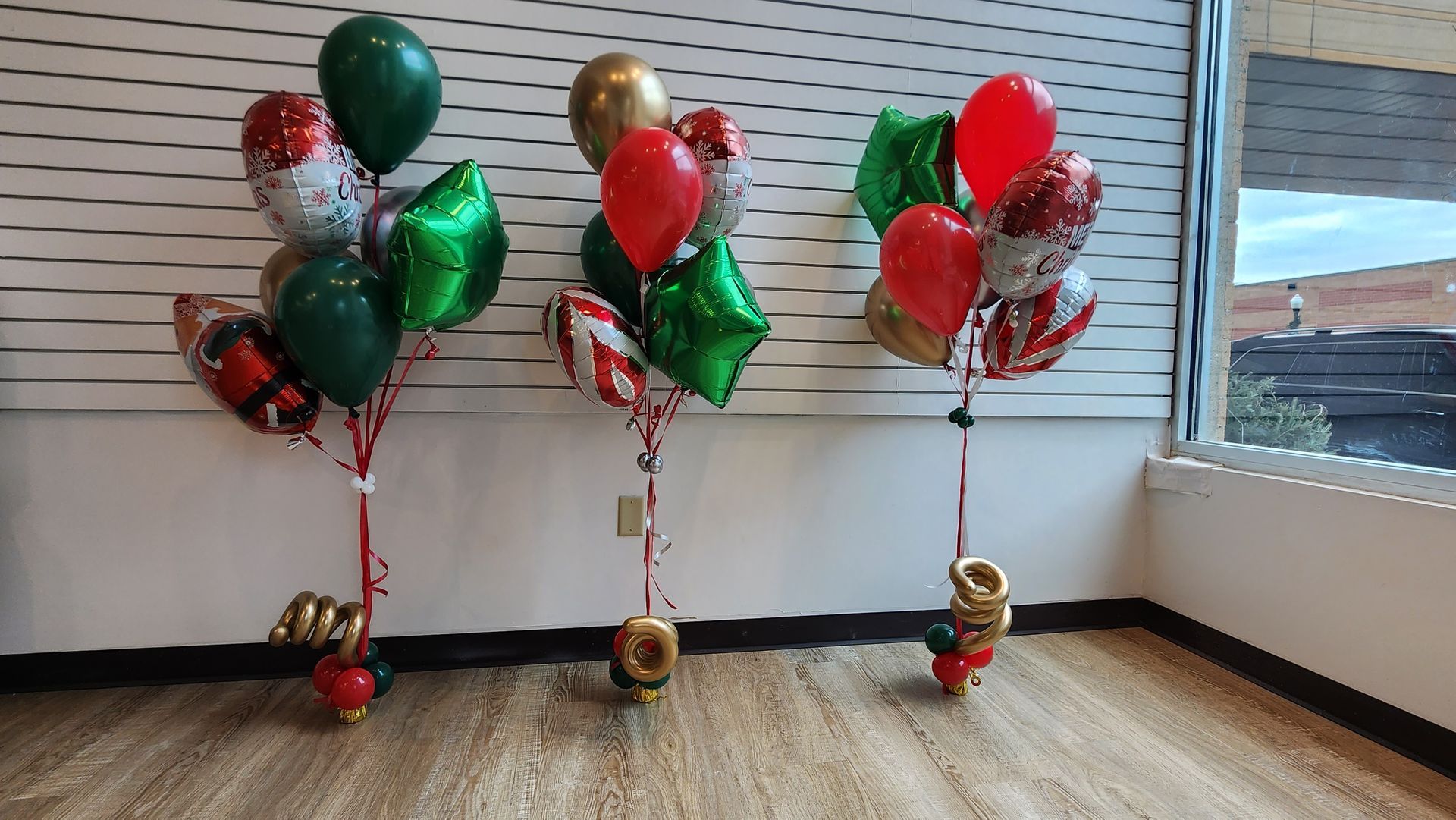 Three christmas balloons are sitting on the floor in a room.