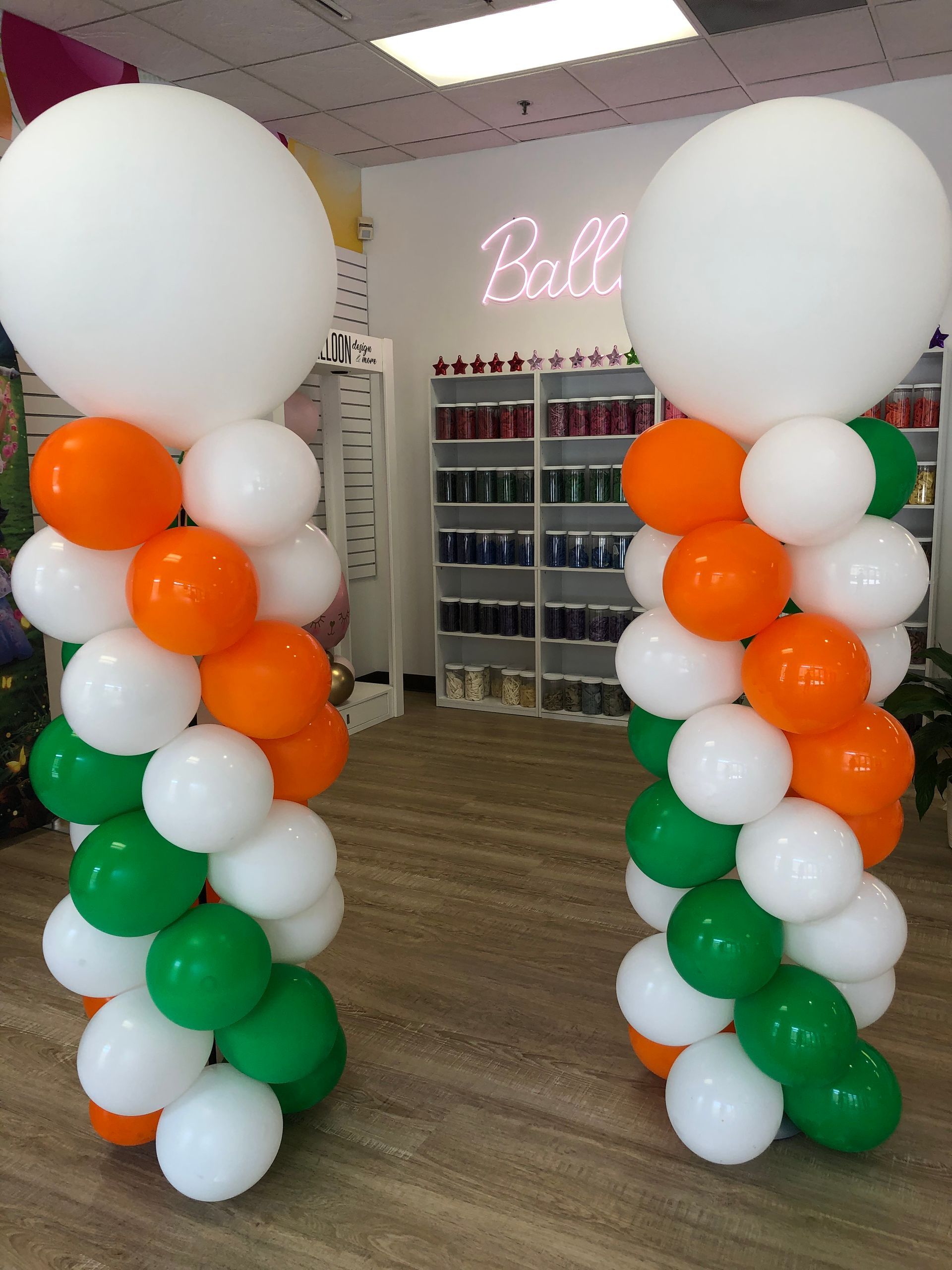 Two columns of balloons in a room with a neon sign that says ball