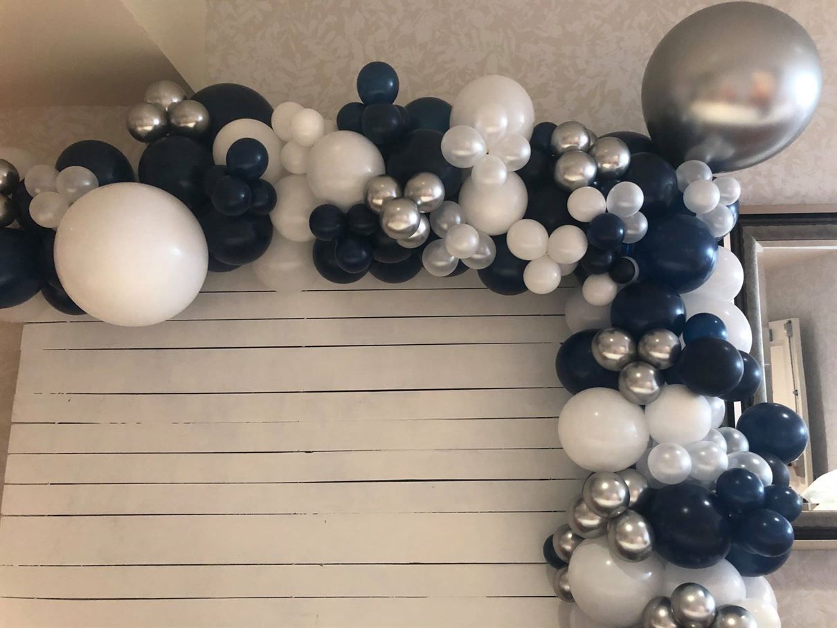 A bunch of blue , white and silver balloons on a white wall