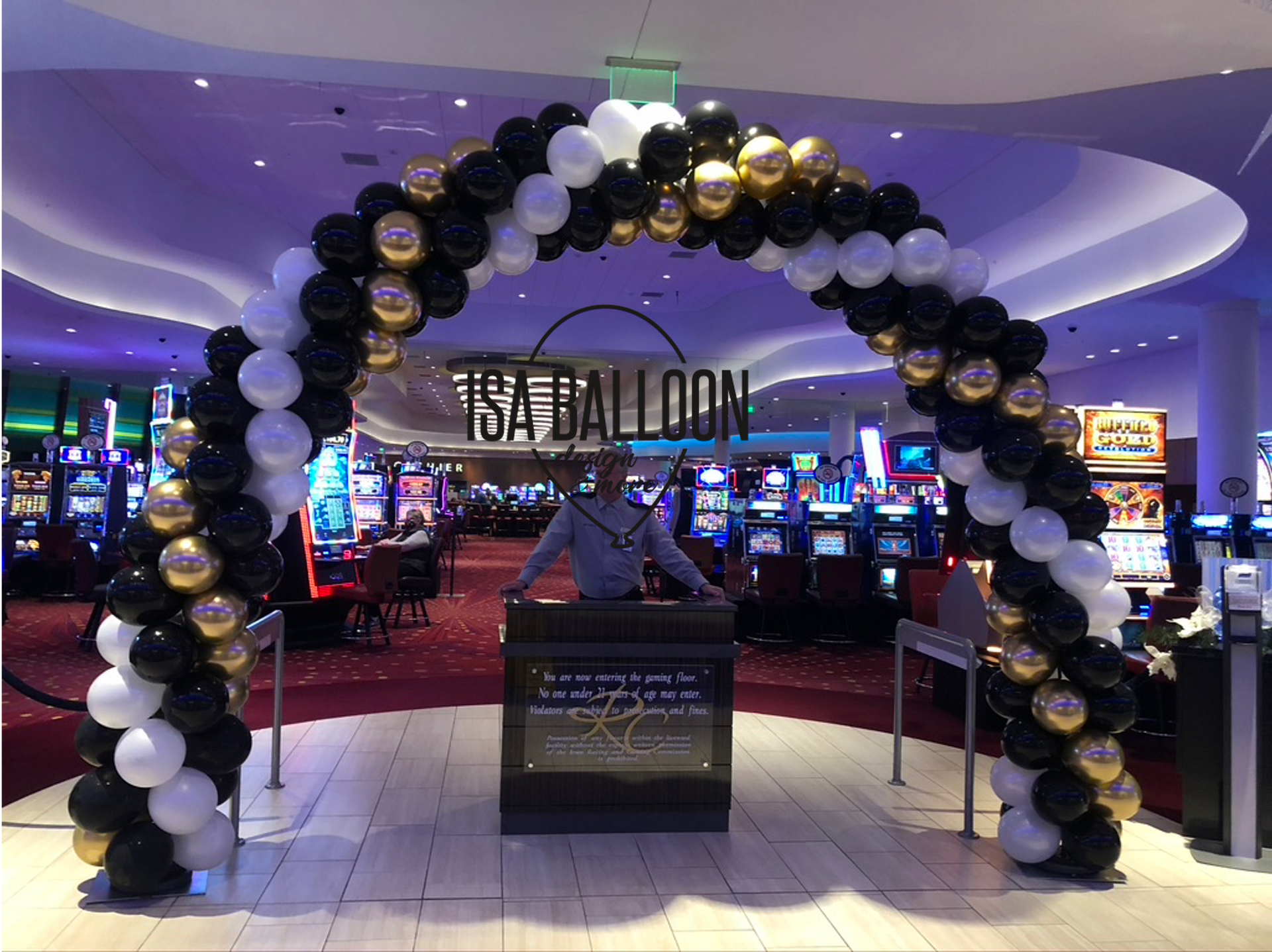 A man is standing in front of a balloon arch in a casino.