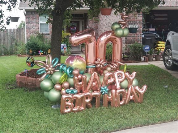 A happy birthday sign with balloons in front of a house.