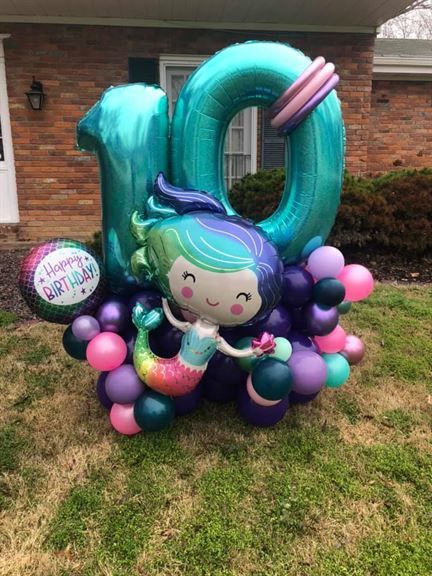 A mermaid balloon is sitting on top of a bunch of balloons in front of a house.