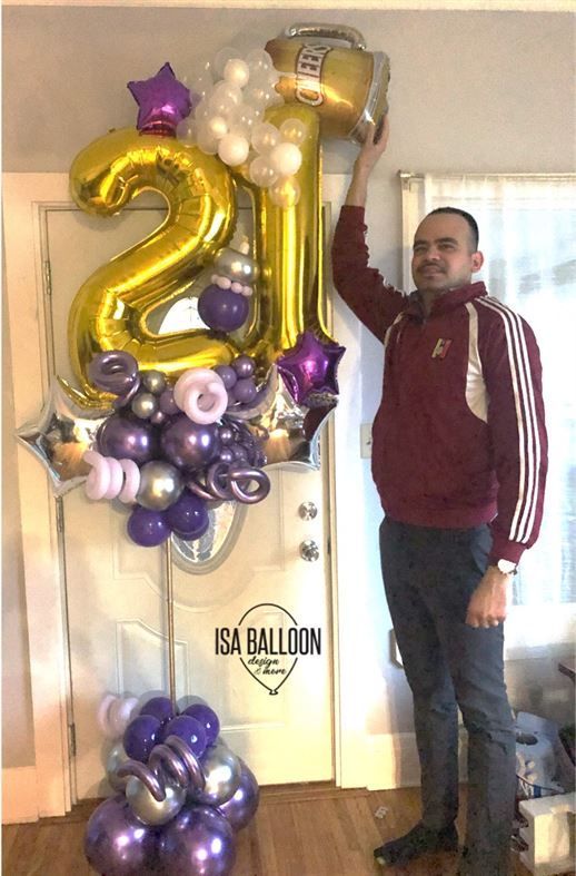 A man is standing next to a bunch of balloons with a number 21 on it.