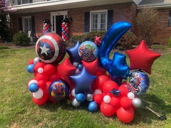 A bunch of balloons are sitting on the grass in front of a house.