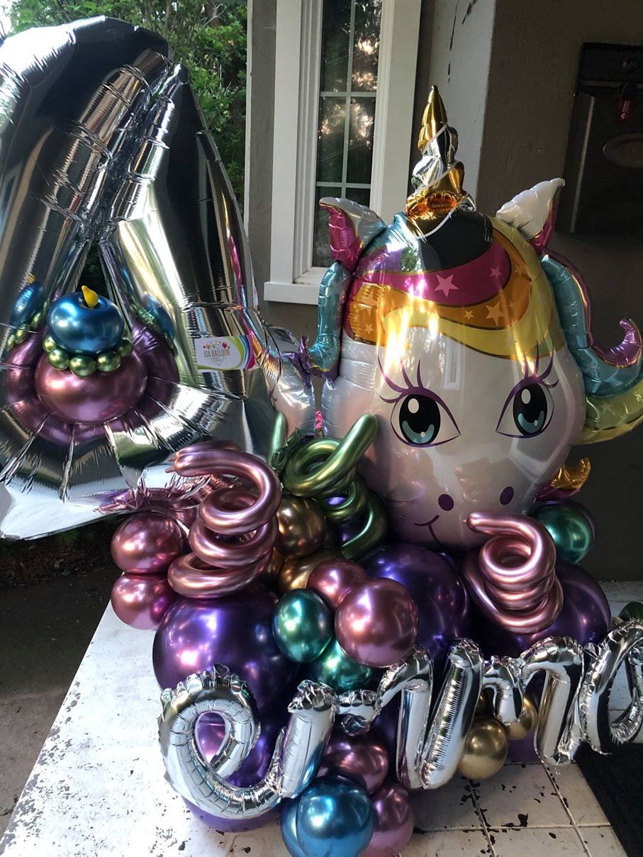 A unicorn balloon is sitting on top of a table surrounded by balloons.