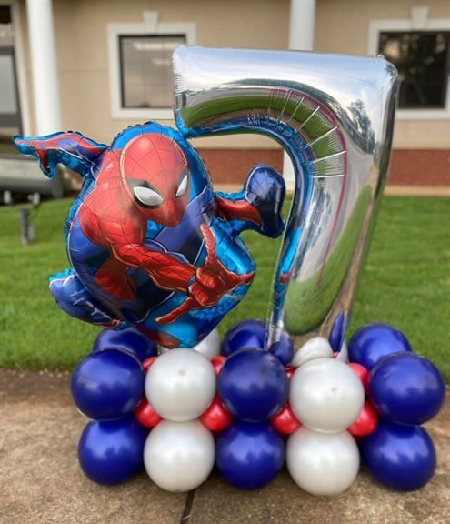 A spiderman balloon is sitting on top of a number 7 balloon