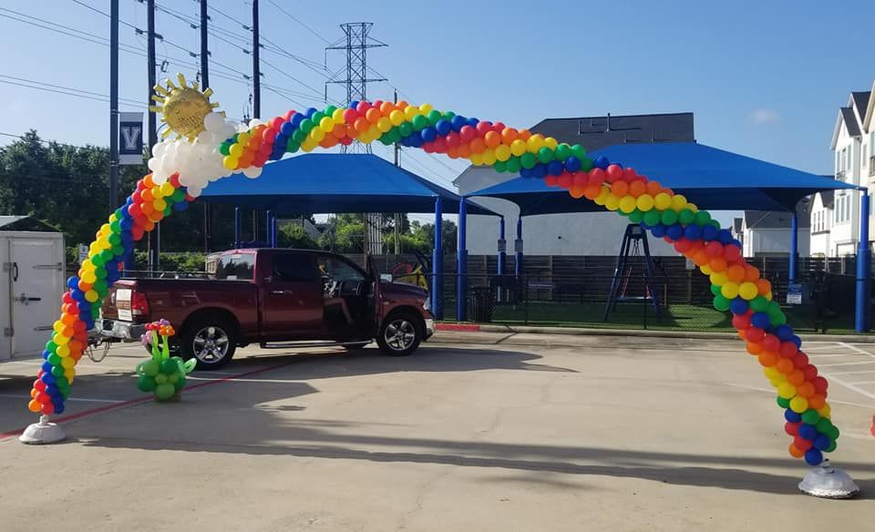 A red truck is parked under a rainbow of balloons in a parking lot.