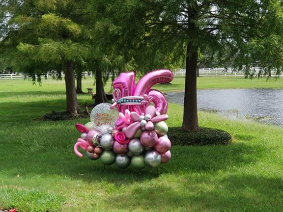 A bunch of pink and silver balloons sitting on top of a lush green field.