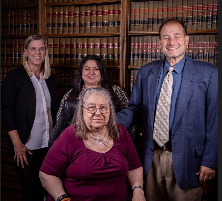 Group of lawyers posing in front of a bookshelf. Smiling, a woman in a wheelchair sits in the front.
