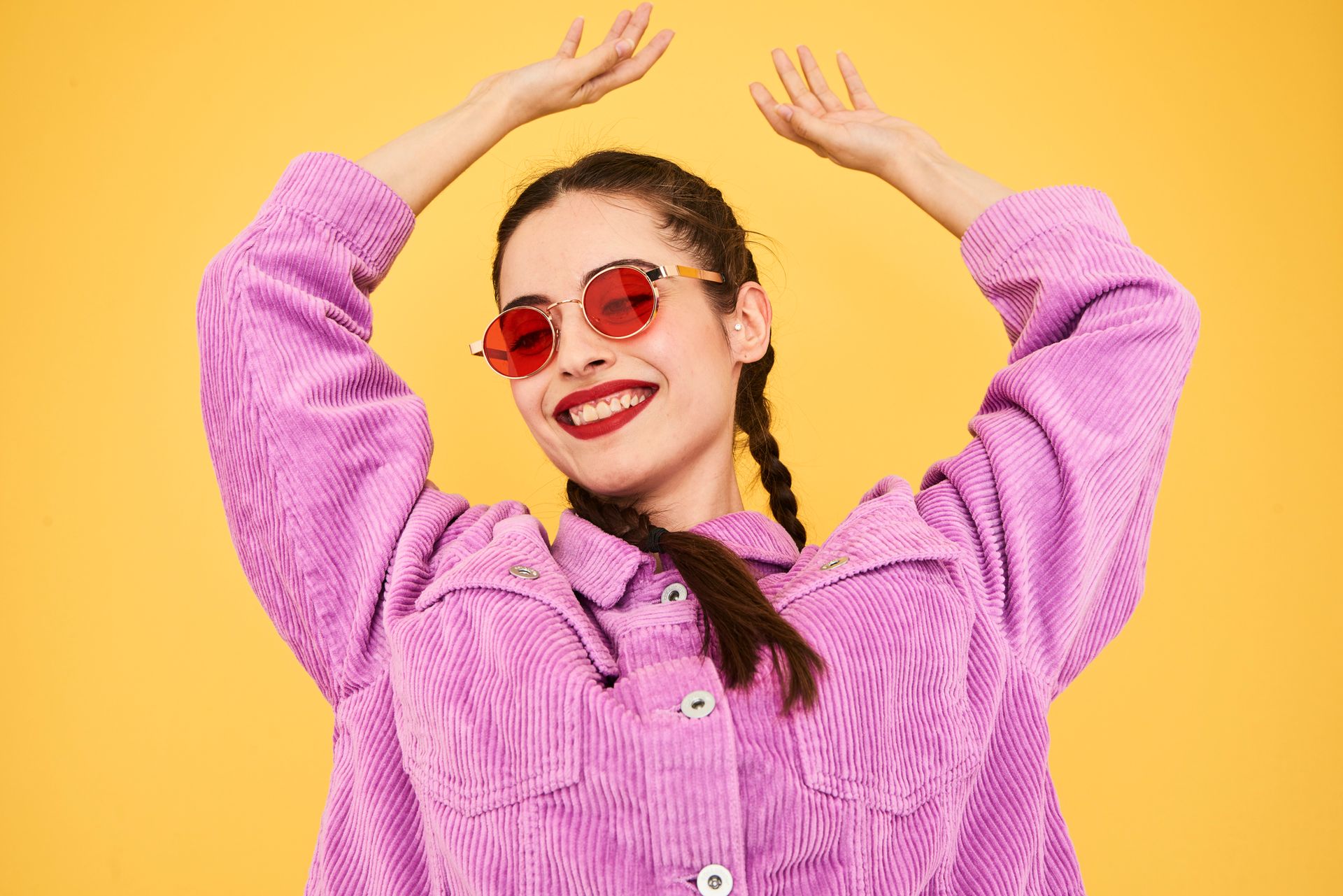 A woman wearing sunglasses and a purple jacket is dancing with her arms in the air.