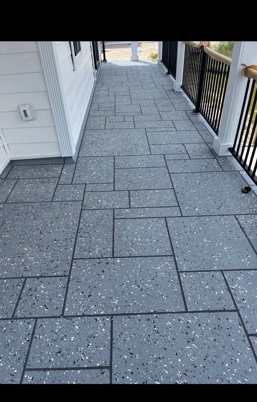 Narrow outdoor walkway with gray paver stones beside a house and black railing