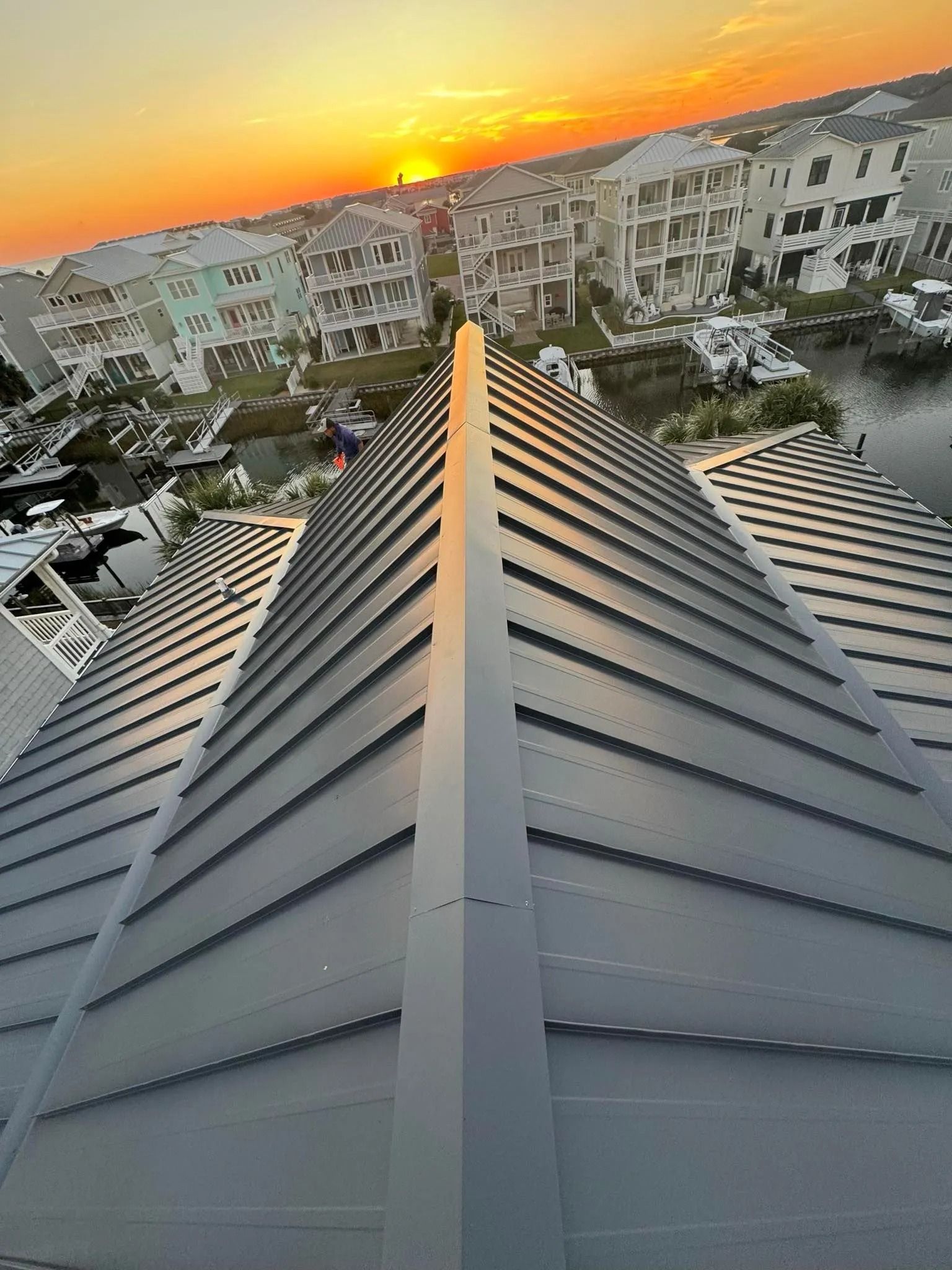 Rooftop view at sunset over apartment buildings, with a metal roof ridge in the foreground.