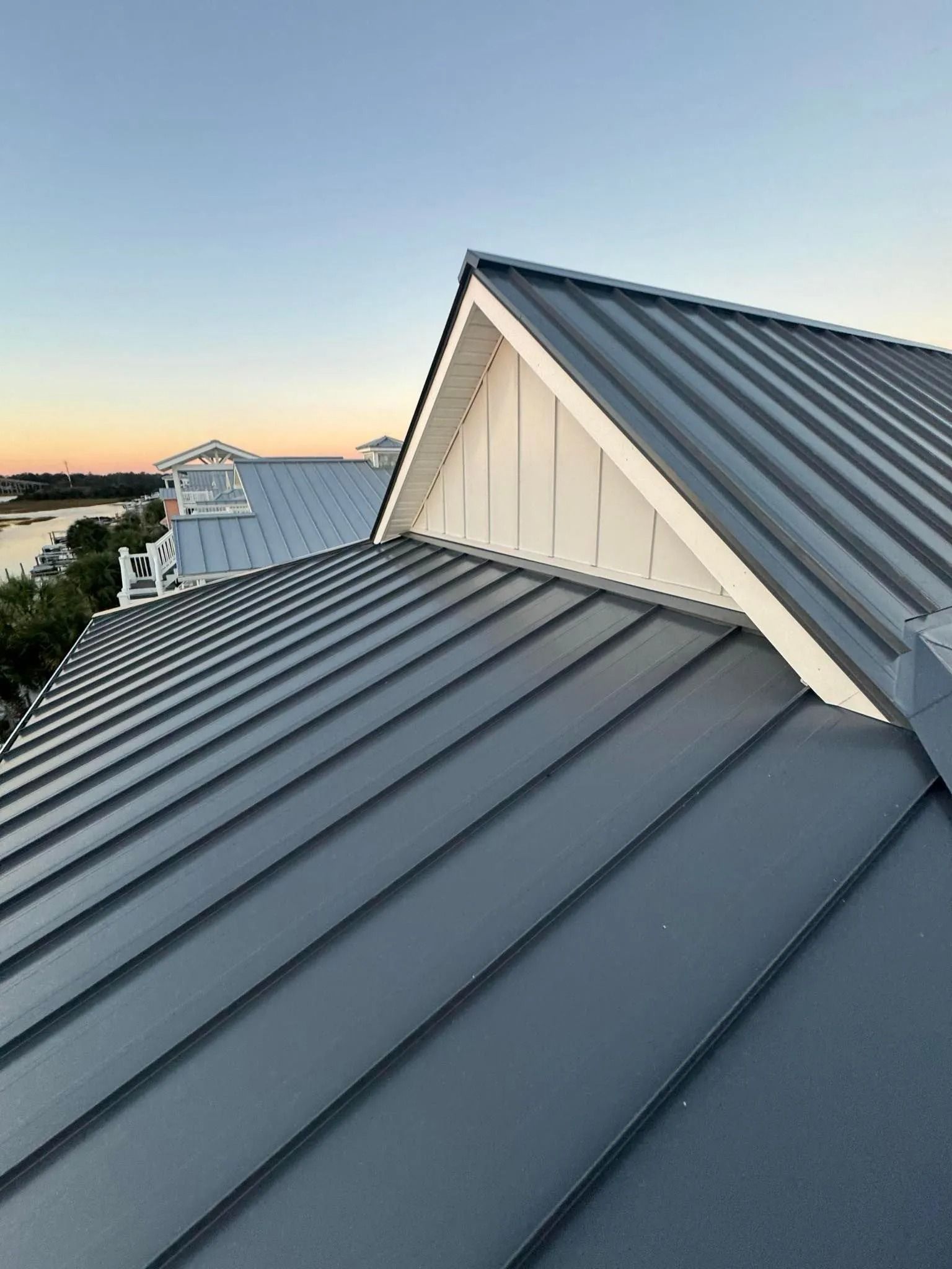 Gray metal rooftops at sunset with a house peak and distant water view