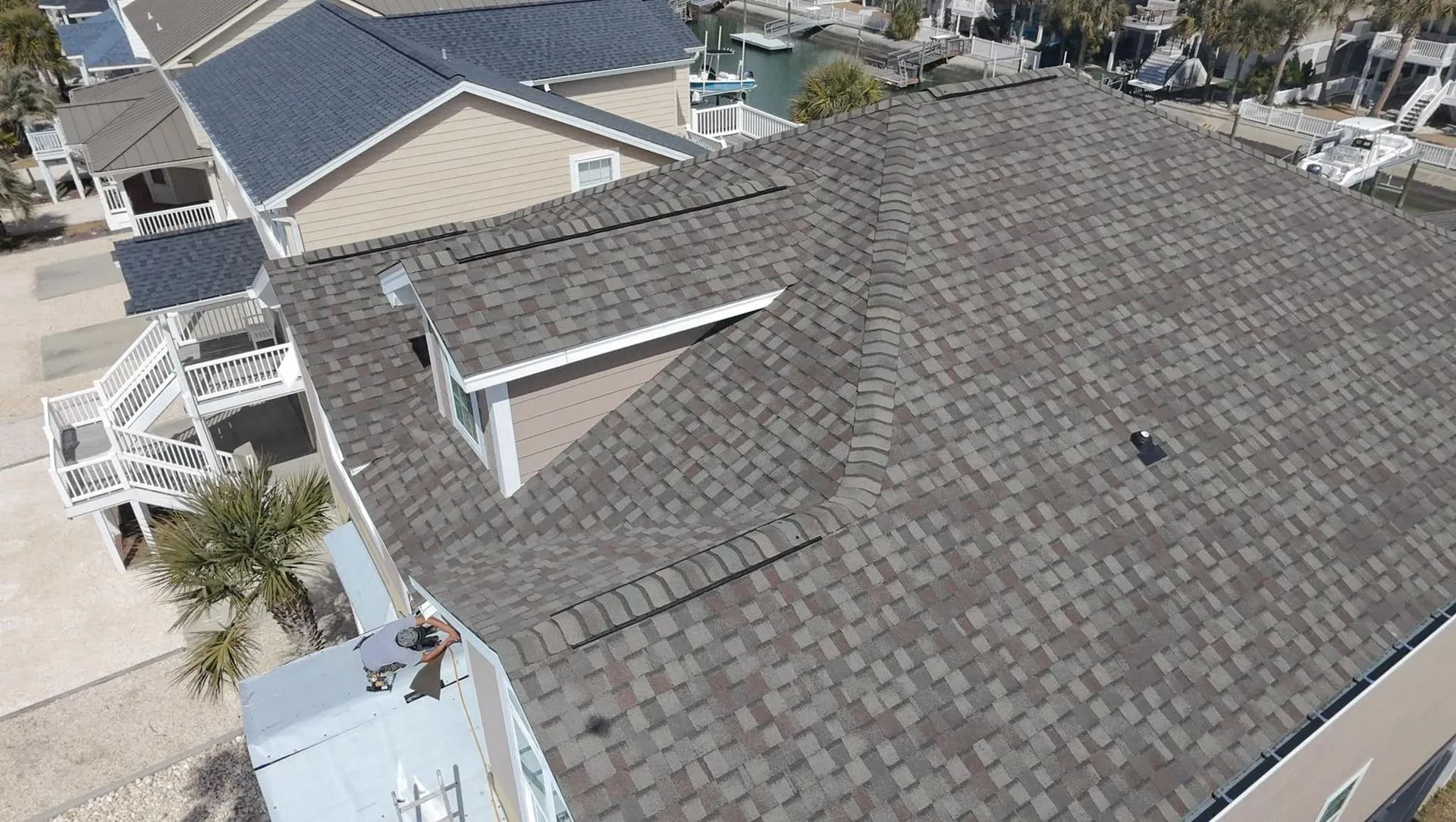 Aerial view of a house roof with gray shingles and a skylight in a suburban neighborhood
