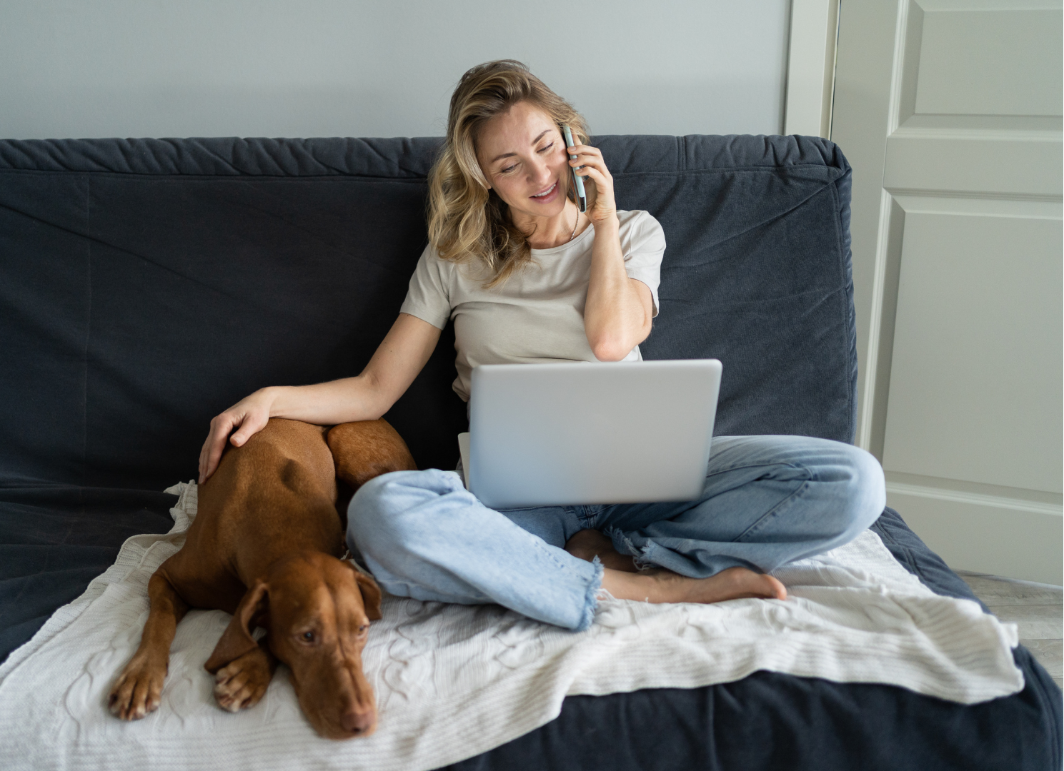 A woman is sitting on a couch with a laptop and talking on a cell phone.