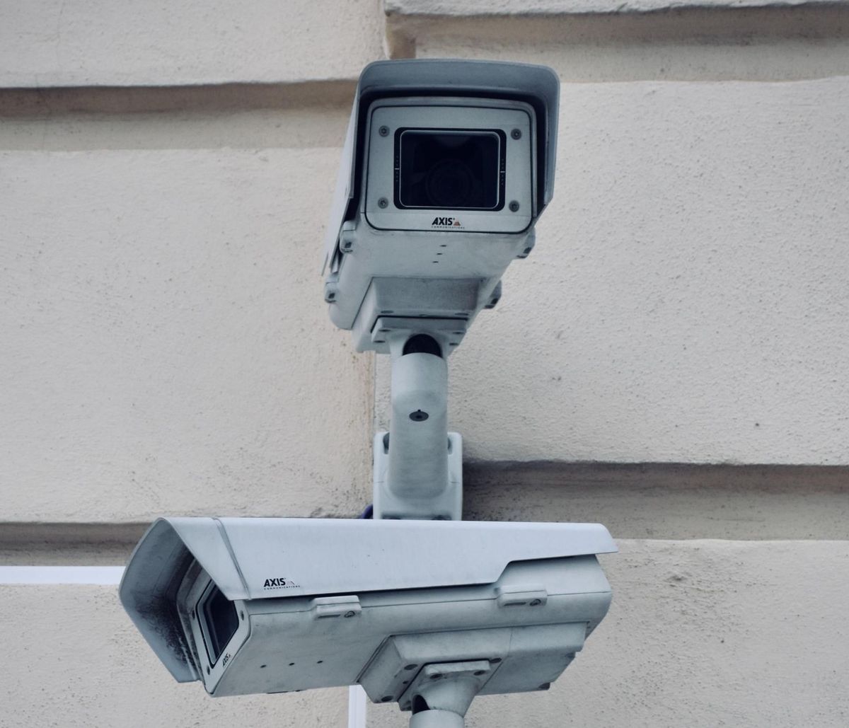 Two white security cameras mounted on a light beige wall.