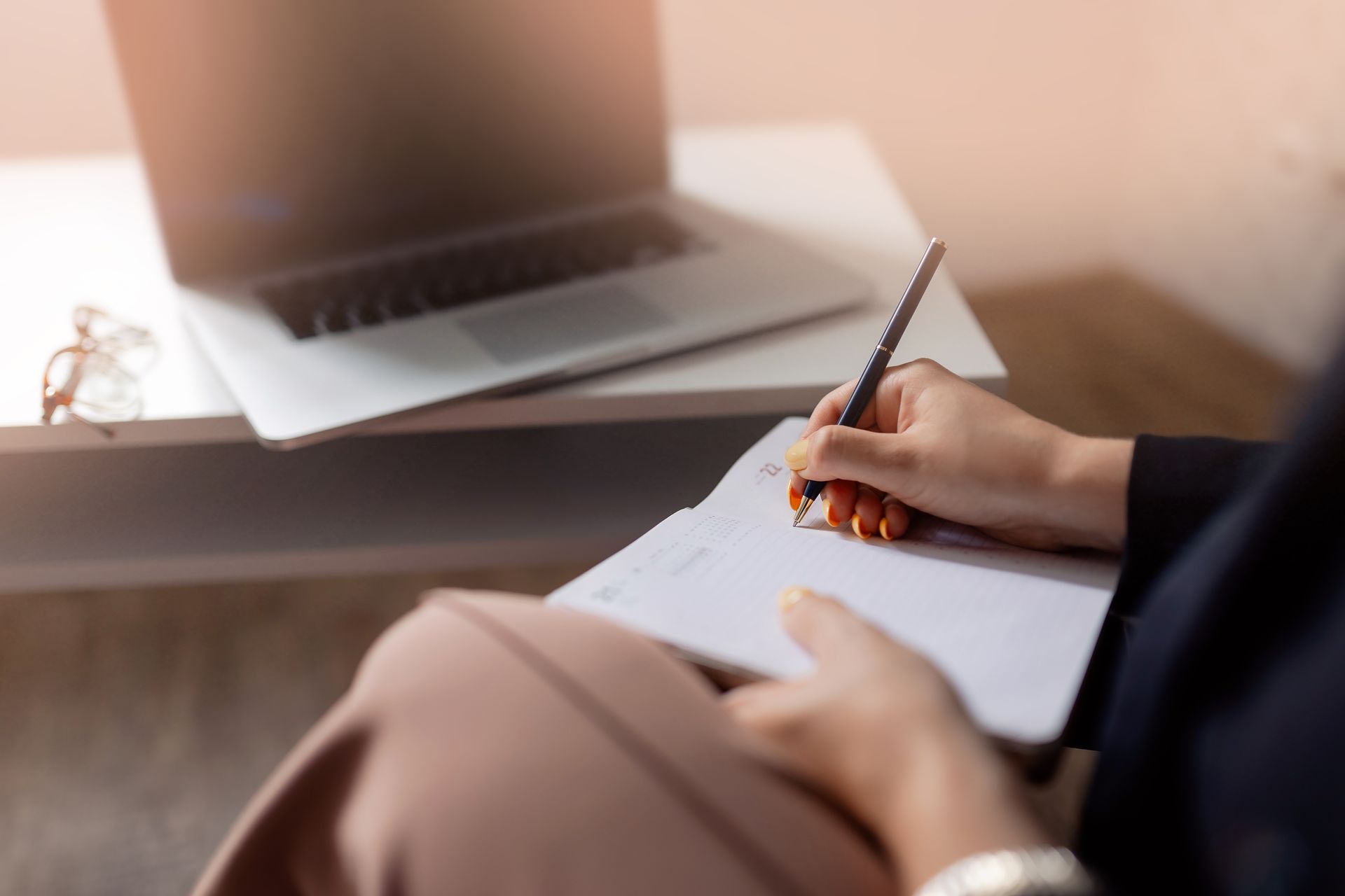 Closeup of a psychiatrist taking notes in notebook during online consultation.