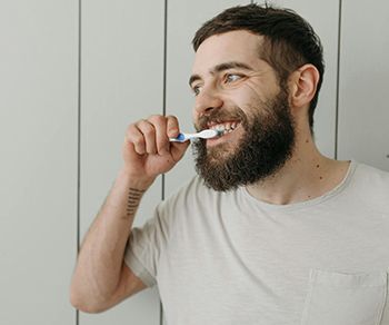 a man with a beard is brushing his teeth with a toothbrush .