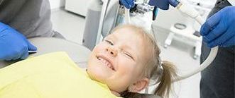 a little girl is laying in a dental chair and smiling .
